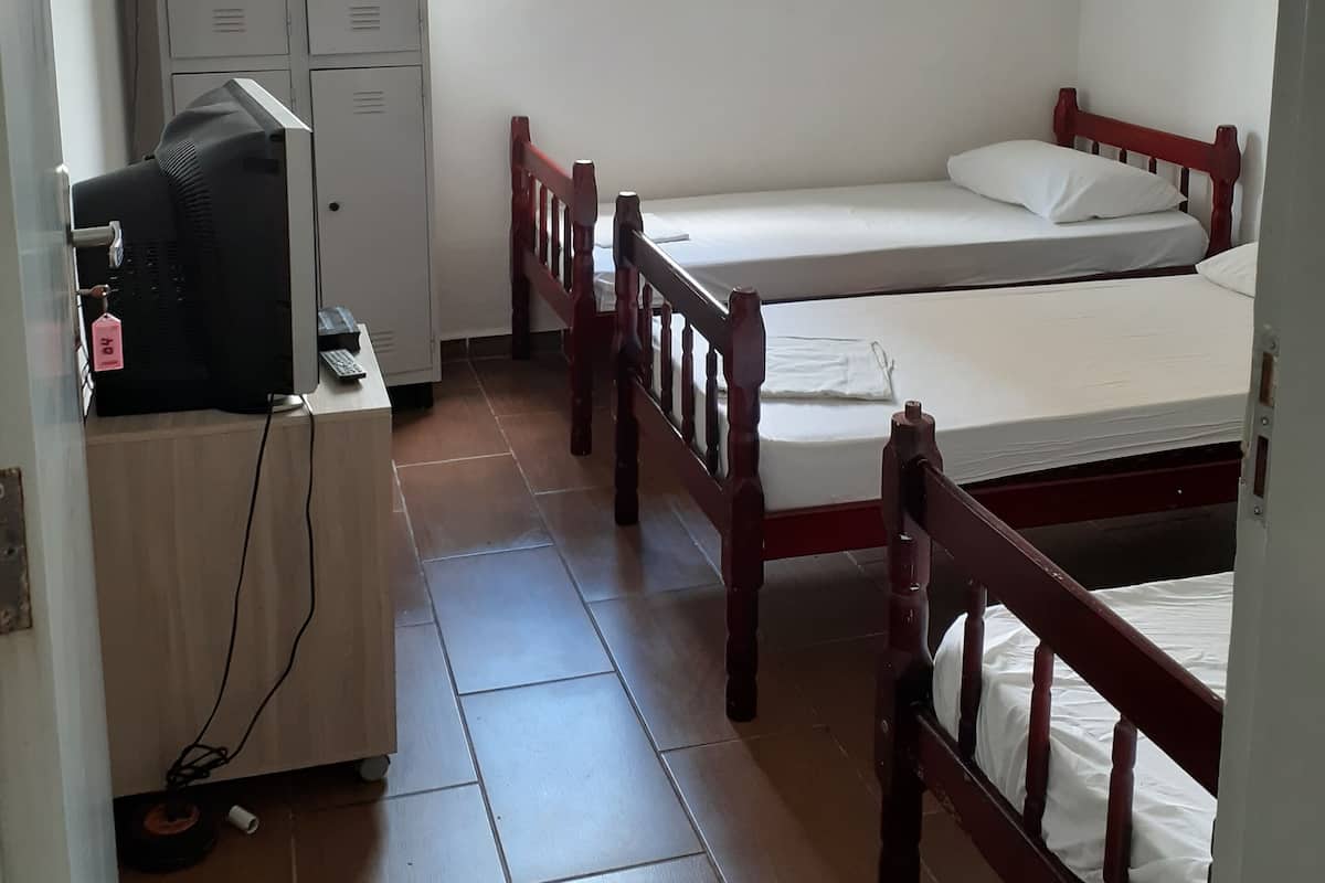 Ein Zimmer mit zwei Holzbetten, einem Schreibtisch mit Computer, einem Kleiderschrank und einem Fenster mit Jalousien.