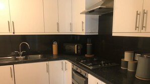 A modern kitchen with white cabinets, a black countertop, a stainless steel sink, a stove, and a microwave.