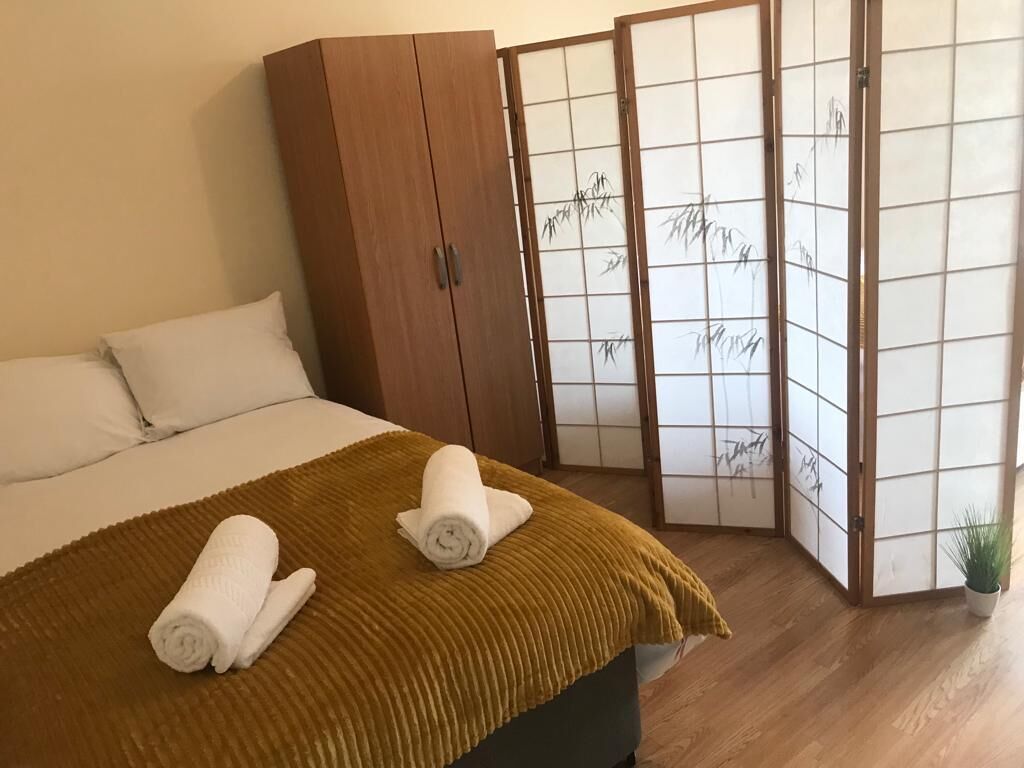 A hotel room with a bed, a wooden wardrobe, a shoji screen, and a potted plant.