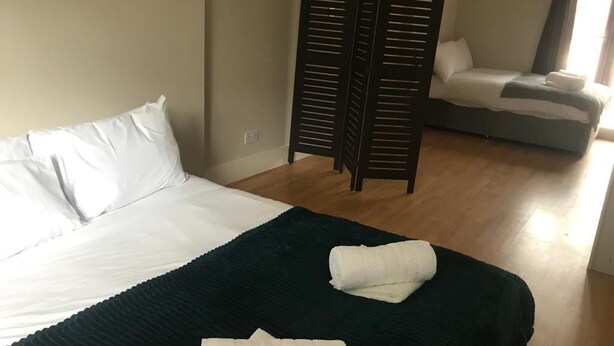 A bedroom with a bed, a dark green blanket, and a wooden partition.