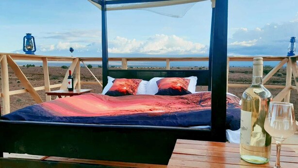 A bed with a sunset view, a bottle of wine, and a glass on a wooden table.