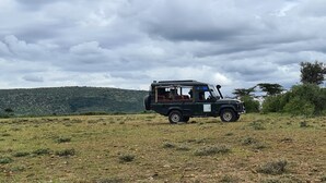 A black safari vehicle parked on a grassy field with a mountainous backdrop.