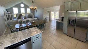 A modern kitchen with a marble countertop, stainless steel appliances, and a dining area with a white railing and chairs. - Oceanside DUCK Beach Home, 5 minute walk to Beach & Shops (Duck)