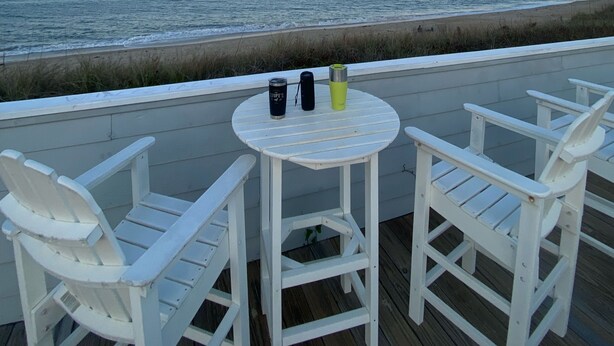 A deck with white chairs and a small table, overlooking a beach with the ocean in the background. - Oceanside DUCK Beach Home, 5 minute walk to Beach & Shops (Duck)