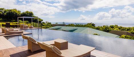 An infinity pool with lounge chairs, a pergola, and a view of the ocean.