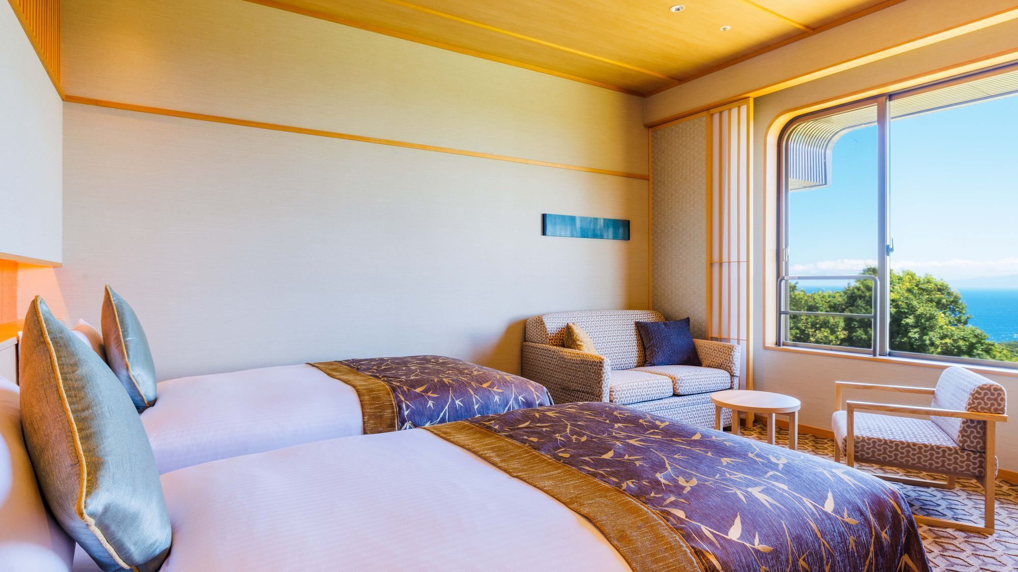A hotel room with two beds, a sofa, a small table, and a view of the ocean.