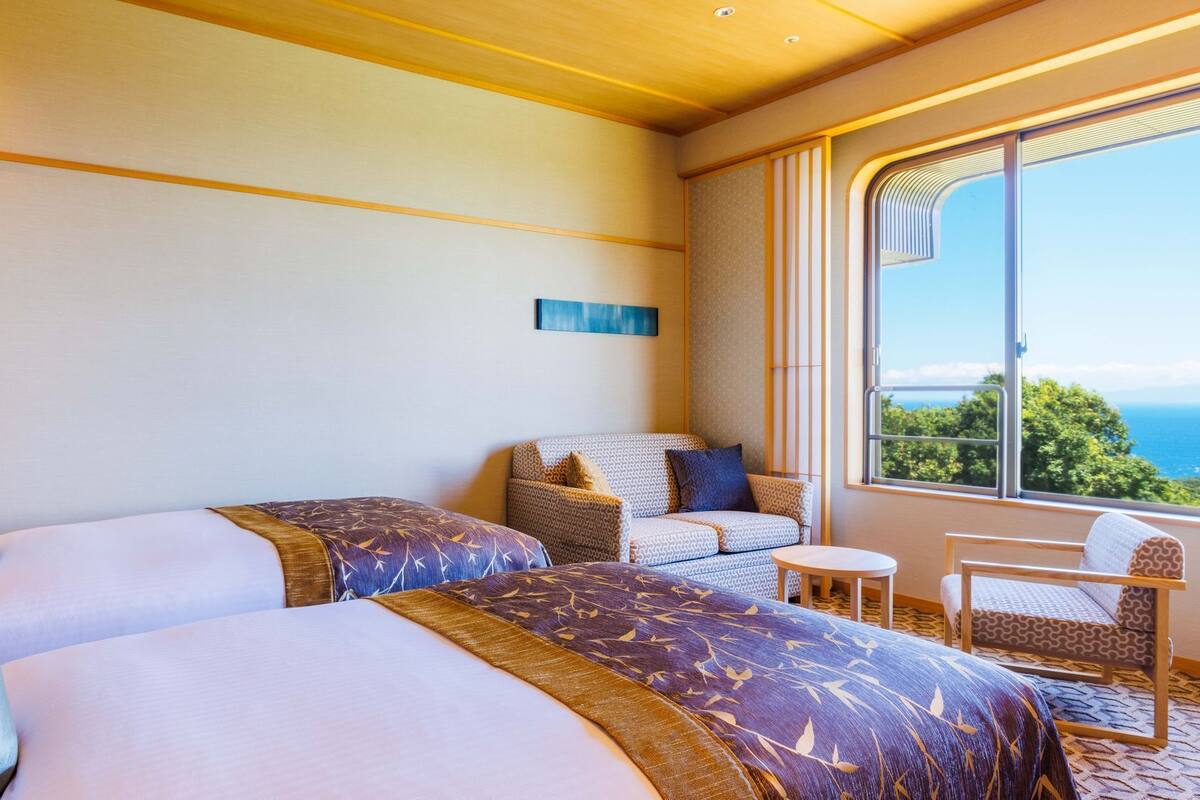 A hotel room with two beds, a sofa, a small table, and a view of the ocean.