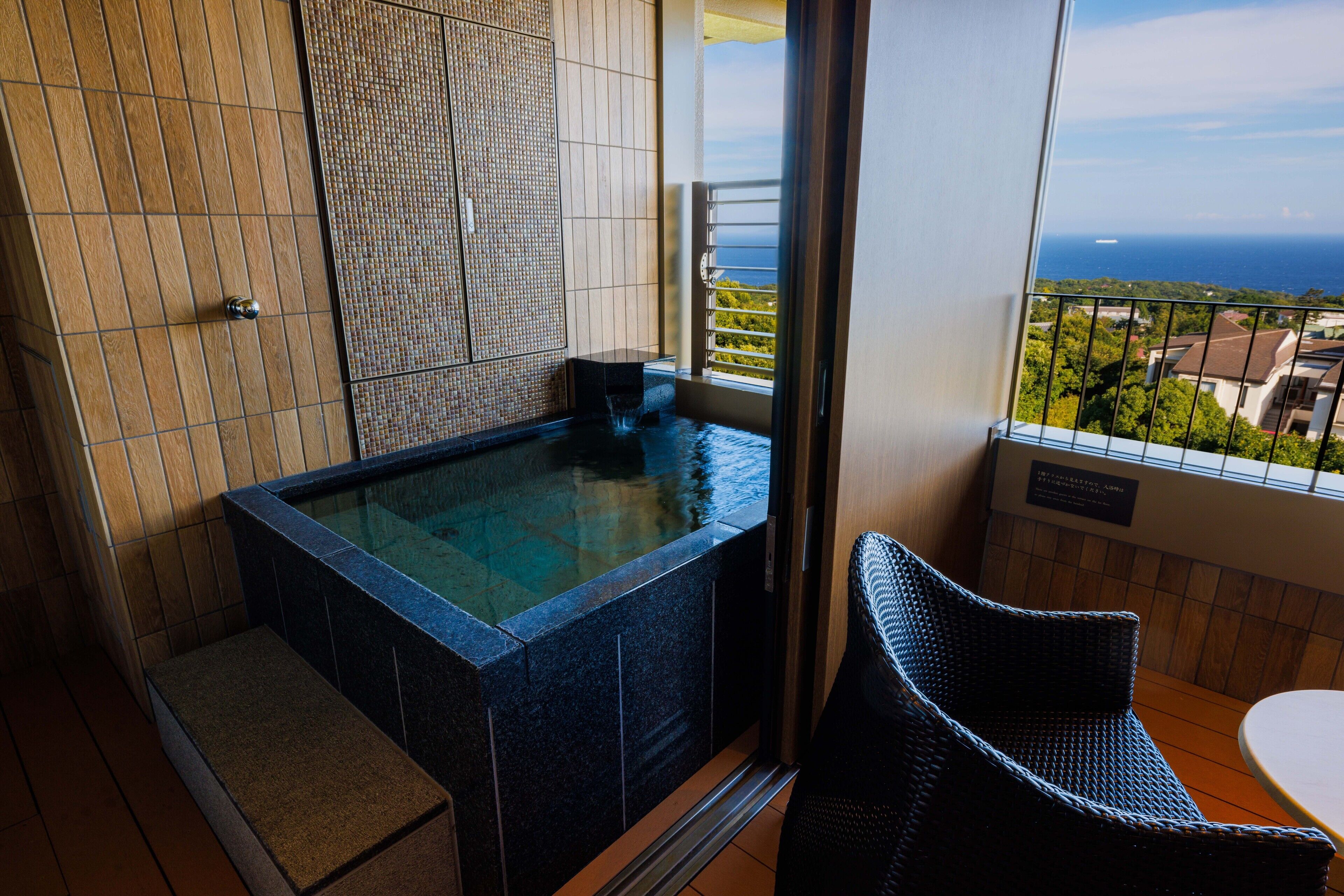 A balcony with a hot tub, a wicker chair, and a view of the ocean.