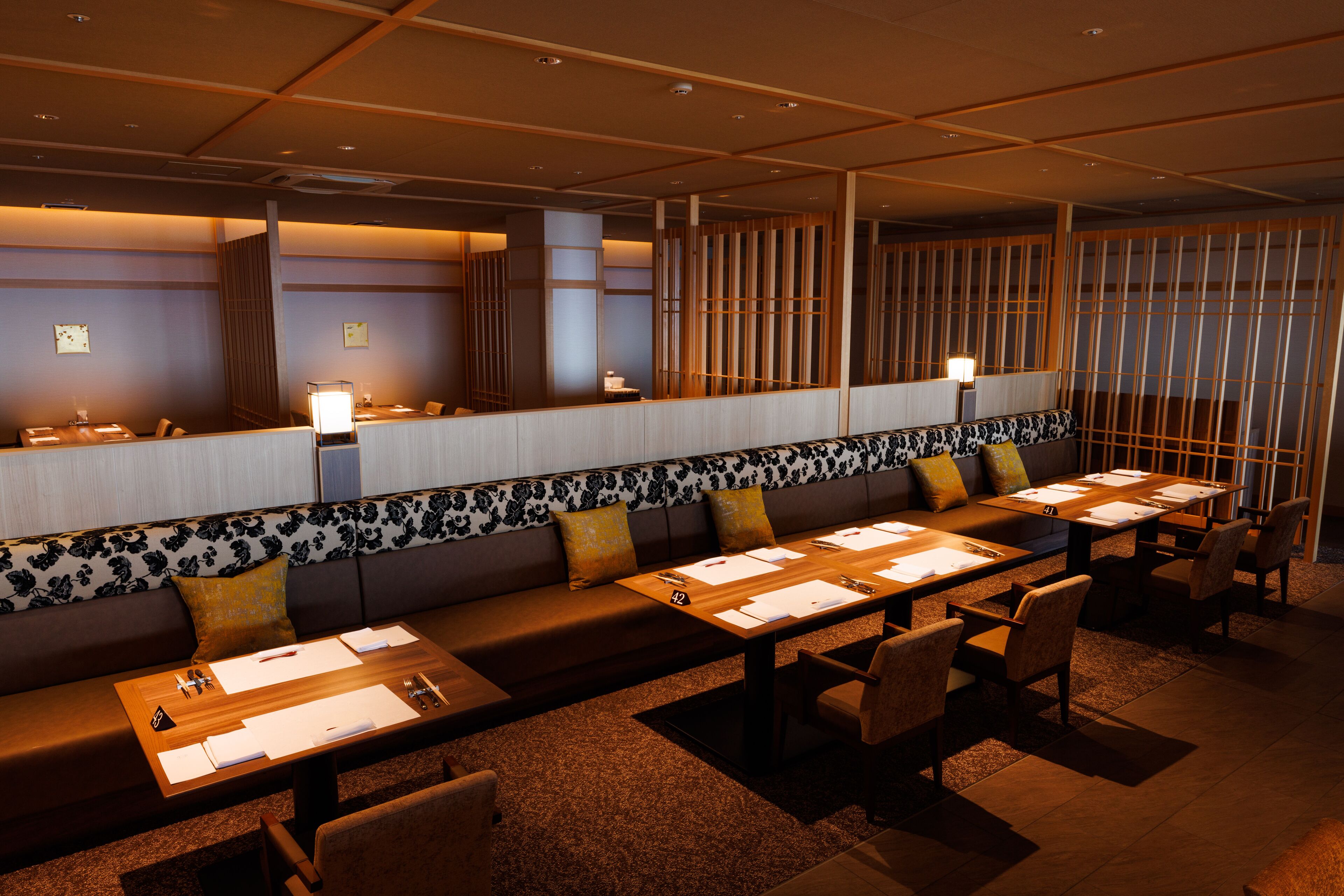 Un restaurante con una barra larga, cabinas y un techo alto con iluminación empotrada.