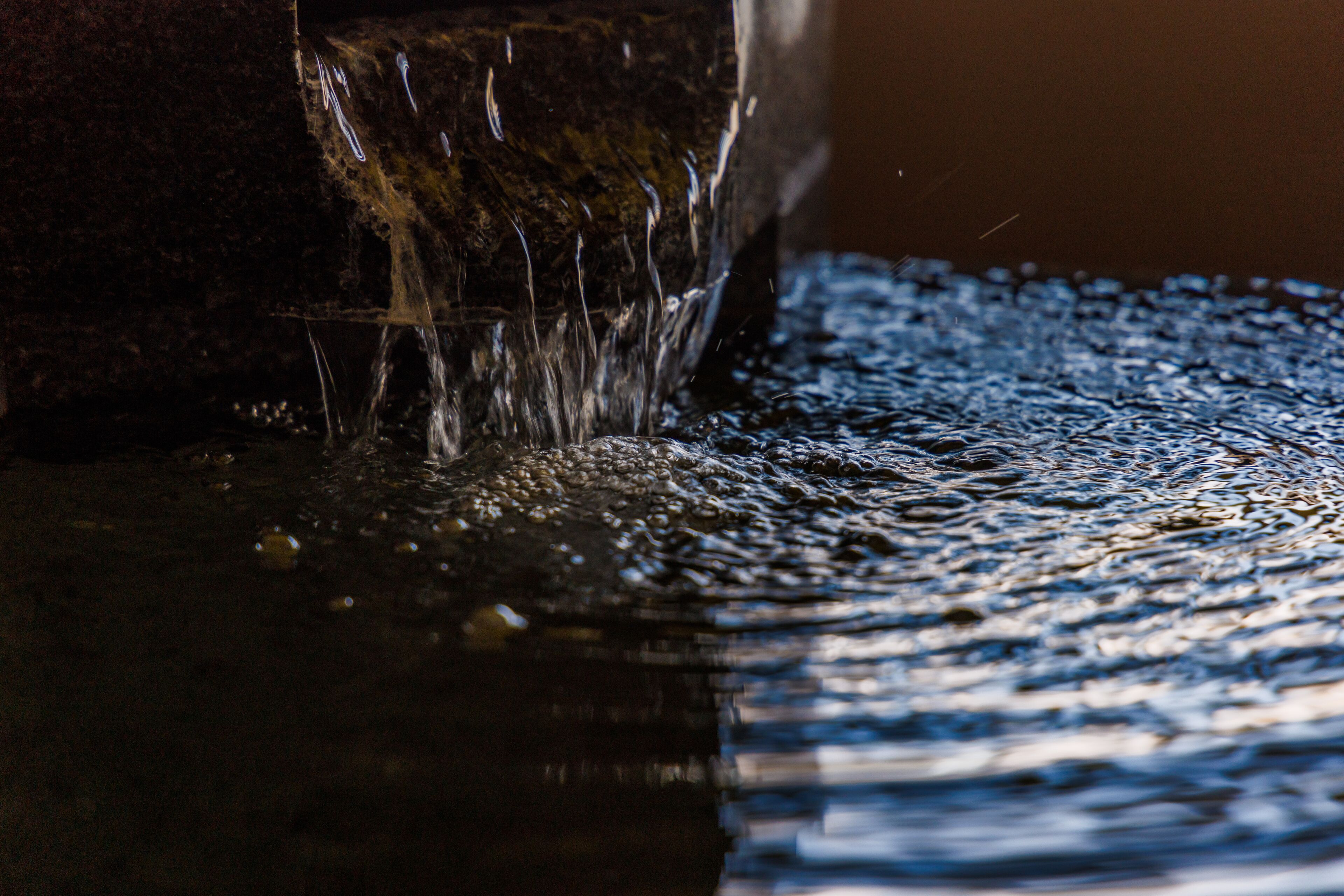A close-up of water flowing over a textured surface, creating ripples and reflections.