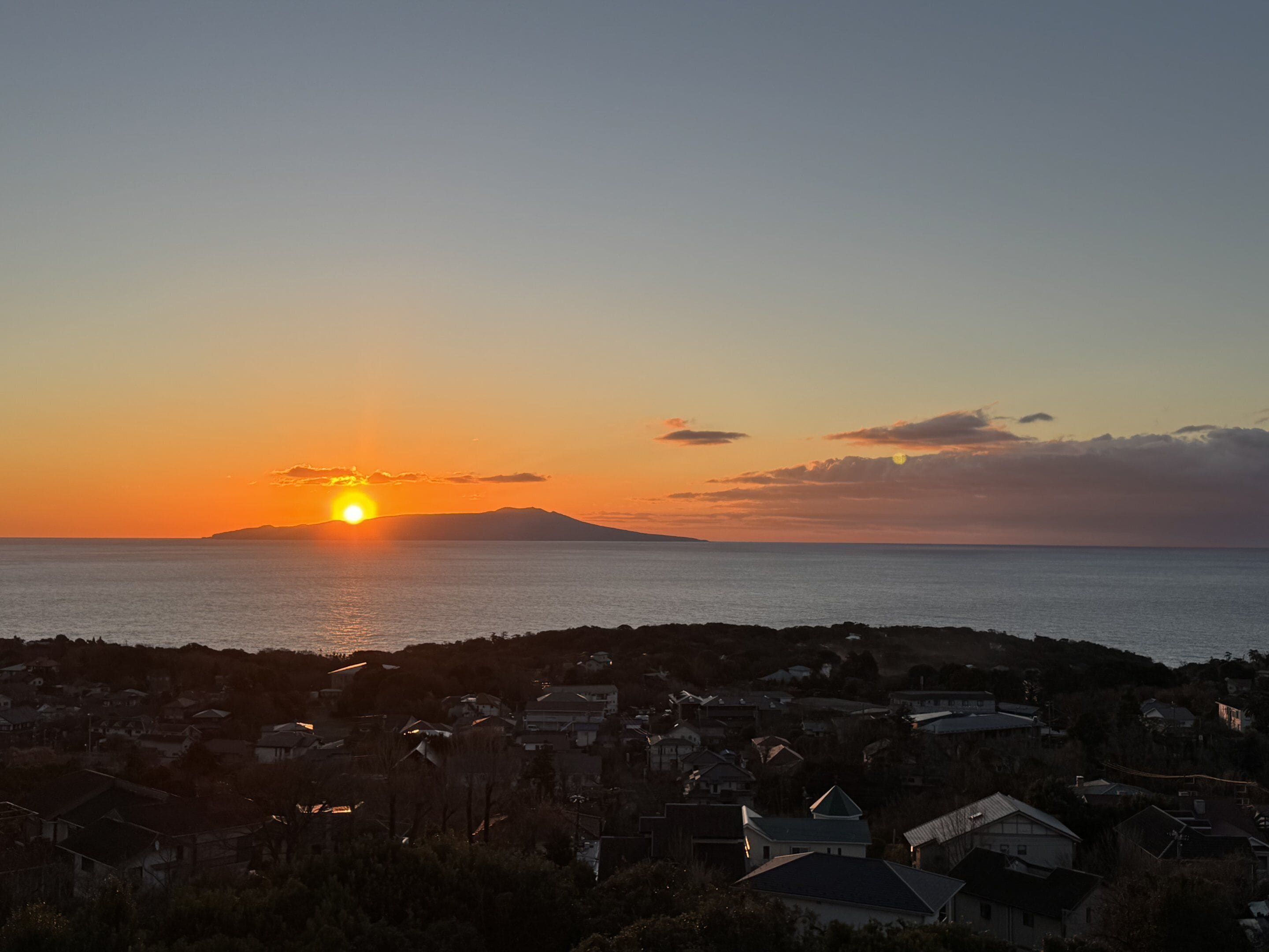 A coastal sunset view with a residential area in the foreground.