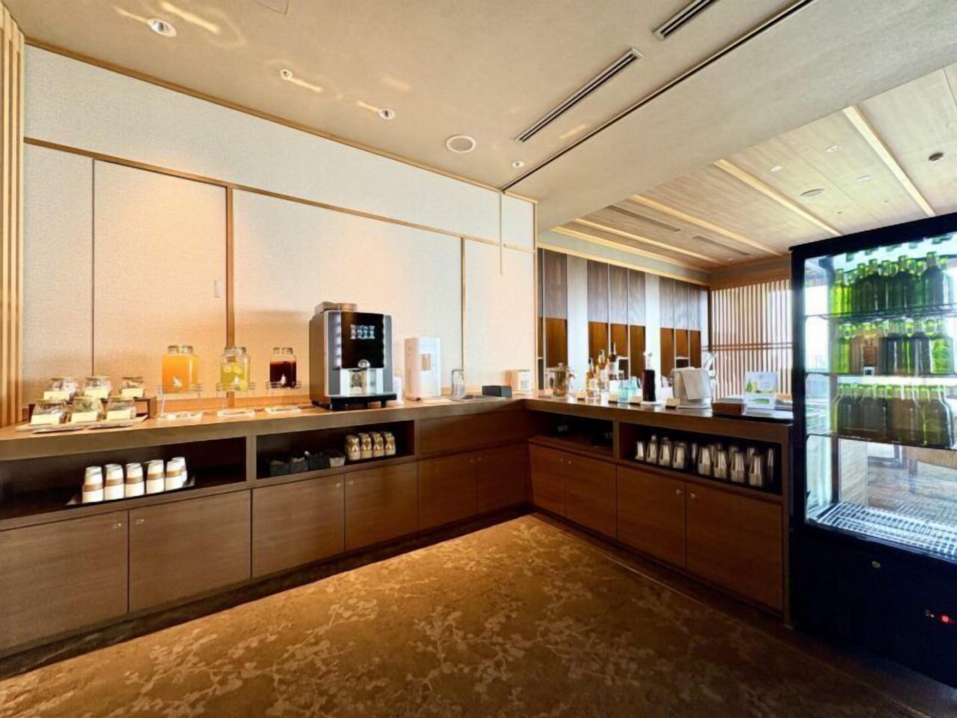 A modern kitchen with a coffee machine, tea station, and a refrigerator.