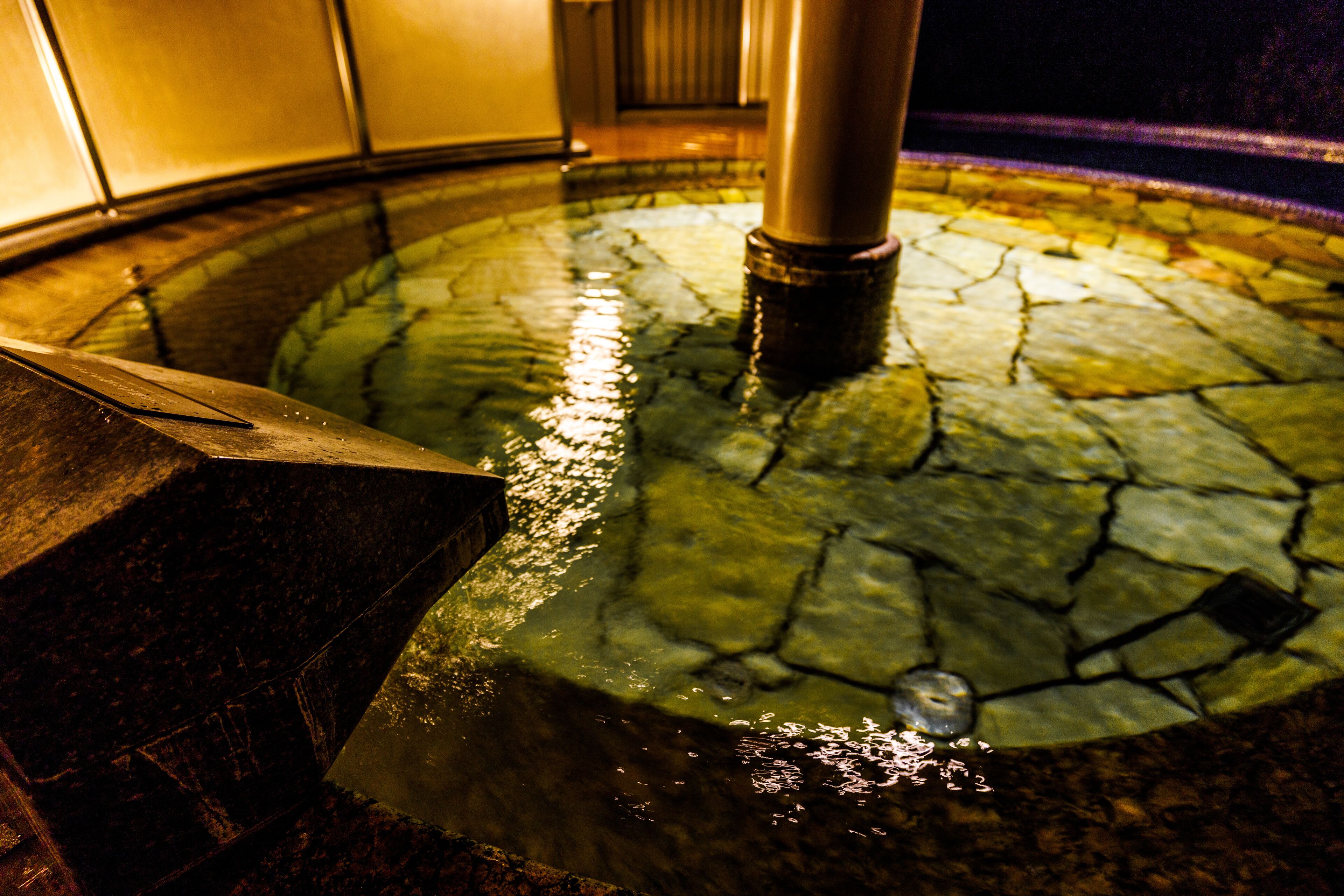 Una piscina circular de piedra con una columna central, rodeada de una zona con azulejos.