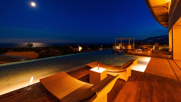 Un área de piscina en la azotea con sillones de descanso y una pequeña mesa, rodeada por una terraza de madera y con vistas panorámicas.