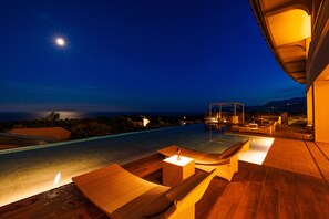 Un área de piscina en la azotea con sillones de descanso y una pequeña mesa, rodeada por una terraza de madera y con vistas panorámicas.