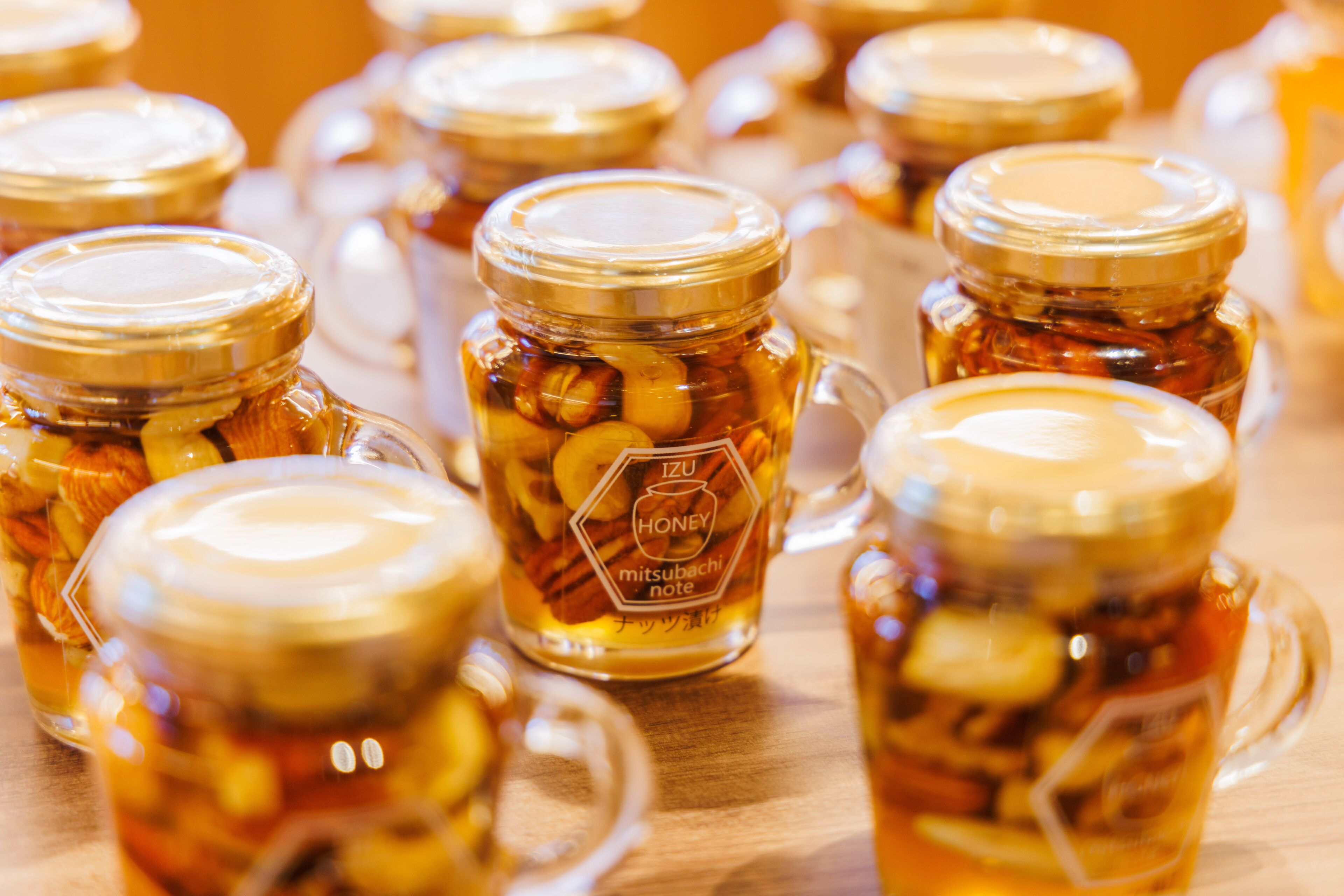 Multiple glass jars with golden lids, each containing a golden liquid and various nuts.