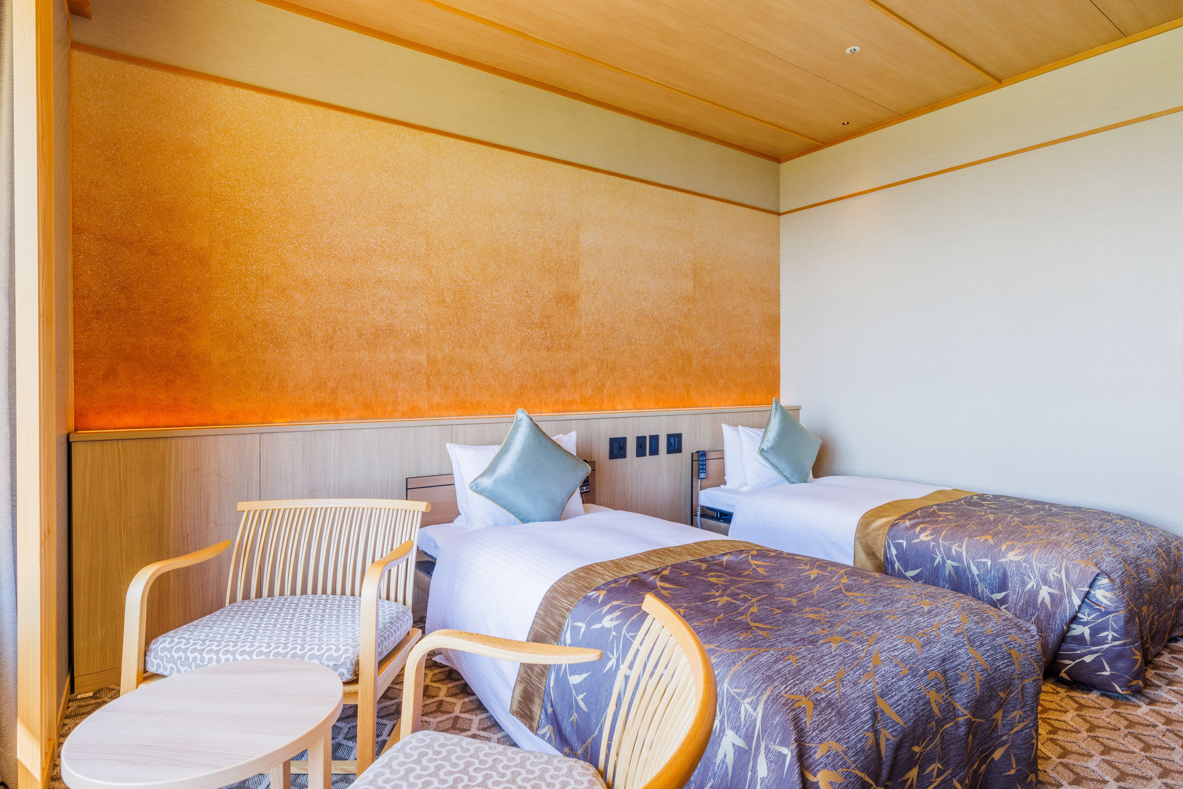 A hotel room with two beds, a wooden chair, a small table, and a wall with a textured finish.