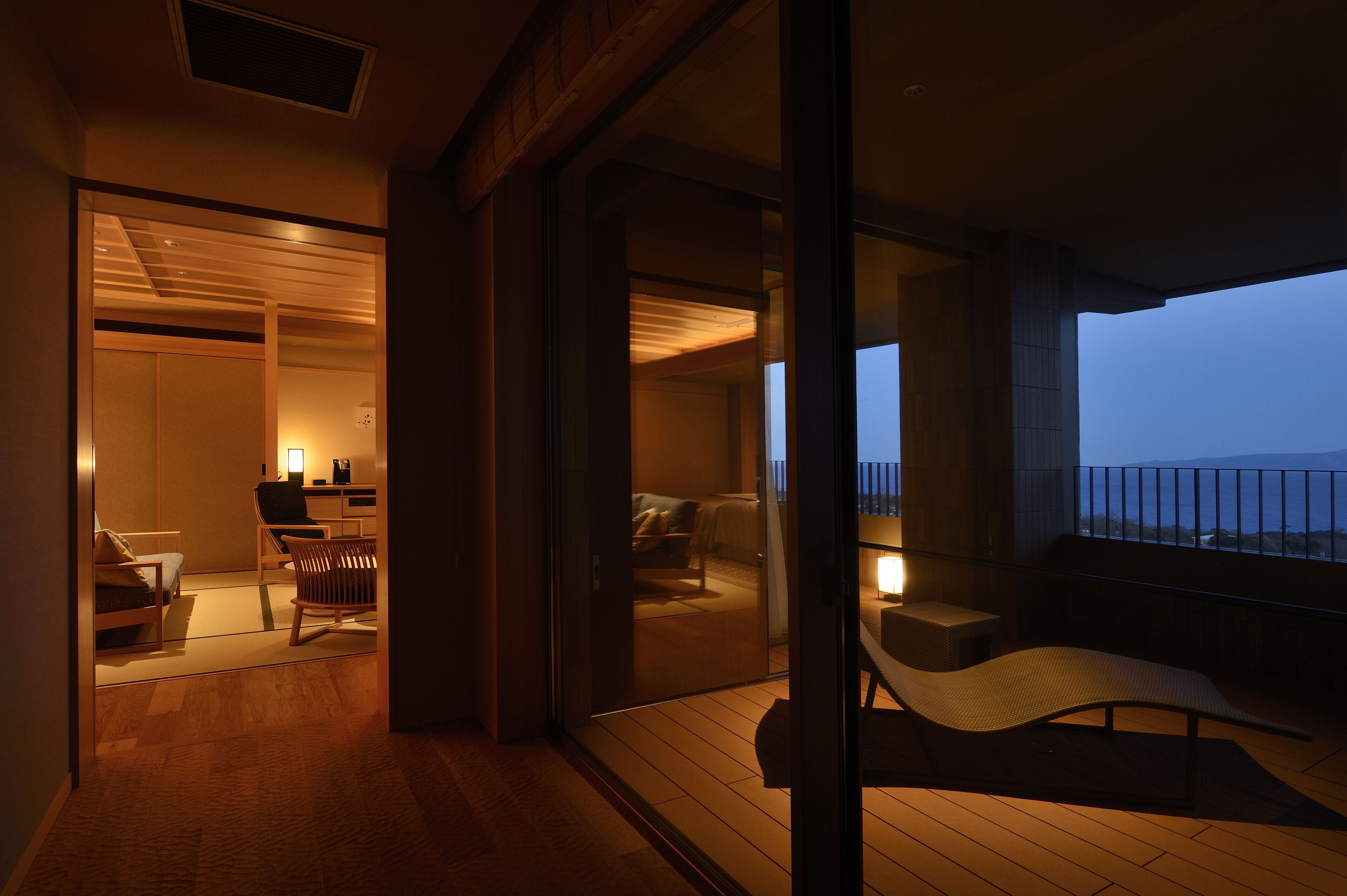 Une chambre d’hôtel moderne avec balcon, plancher en bois et vue sur la mer au crépuscule.