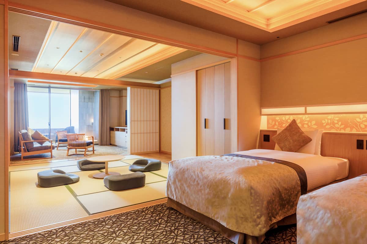 Une chambre d’hôtel avec un sol recouvert de tatamis, un lit de style japonais traditionnel, un canapé et une vue sur la ville.