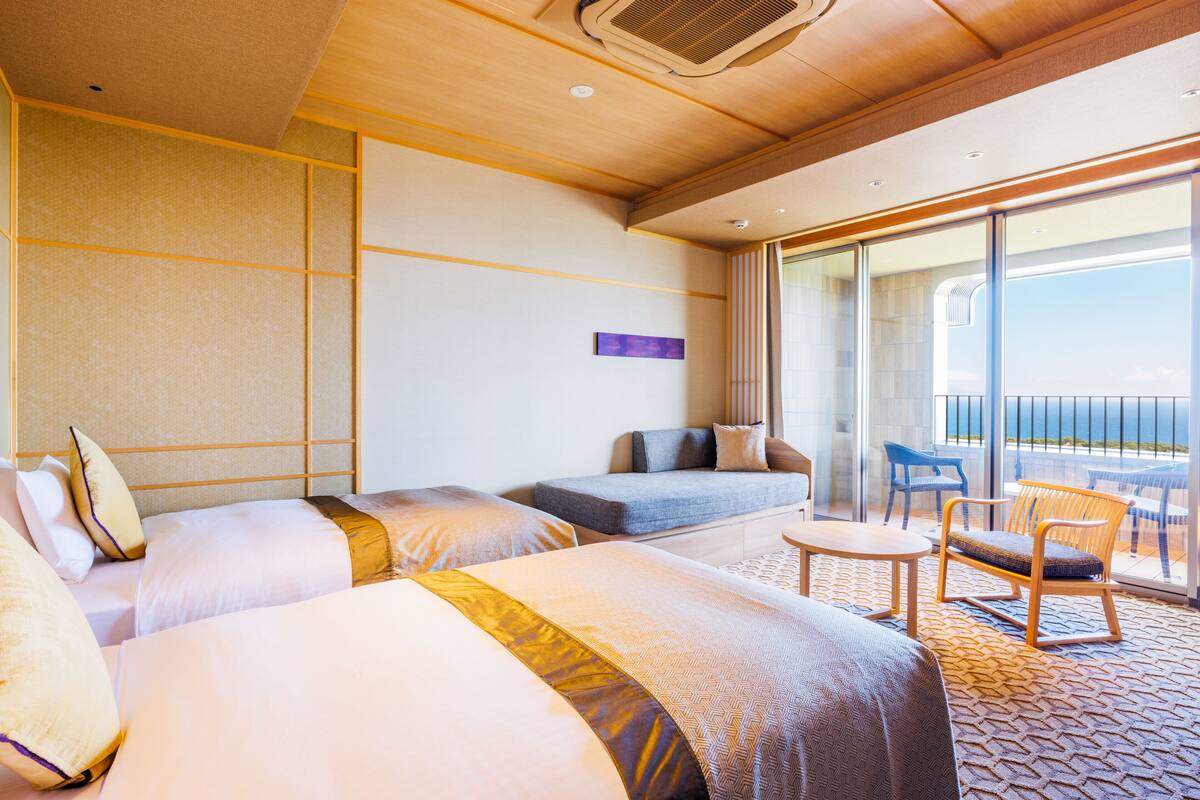 Une chambre d’hôtel avec deux lits, un canapé, une petite table et un balcon équipé de chaises.
