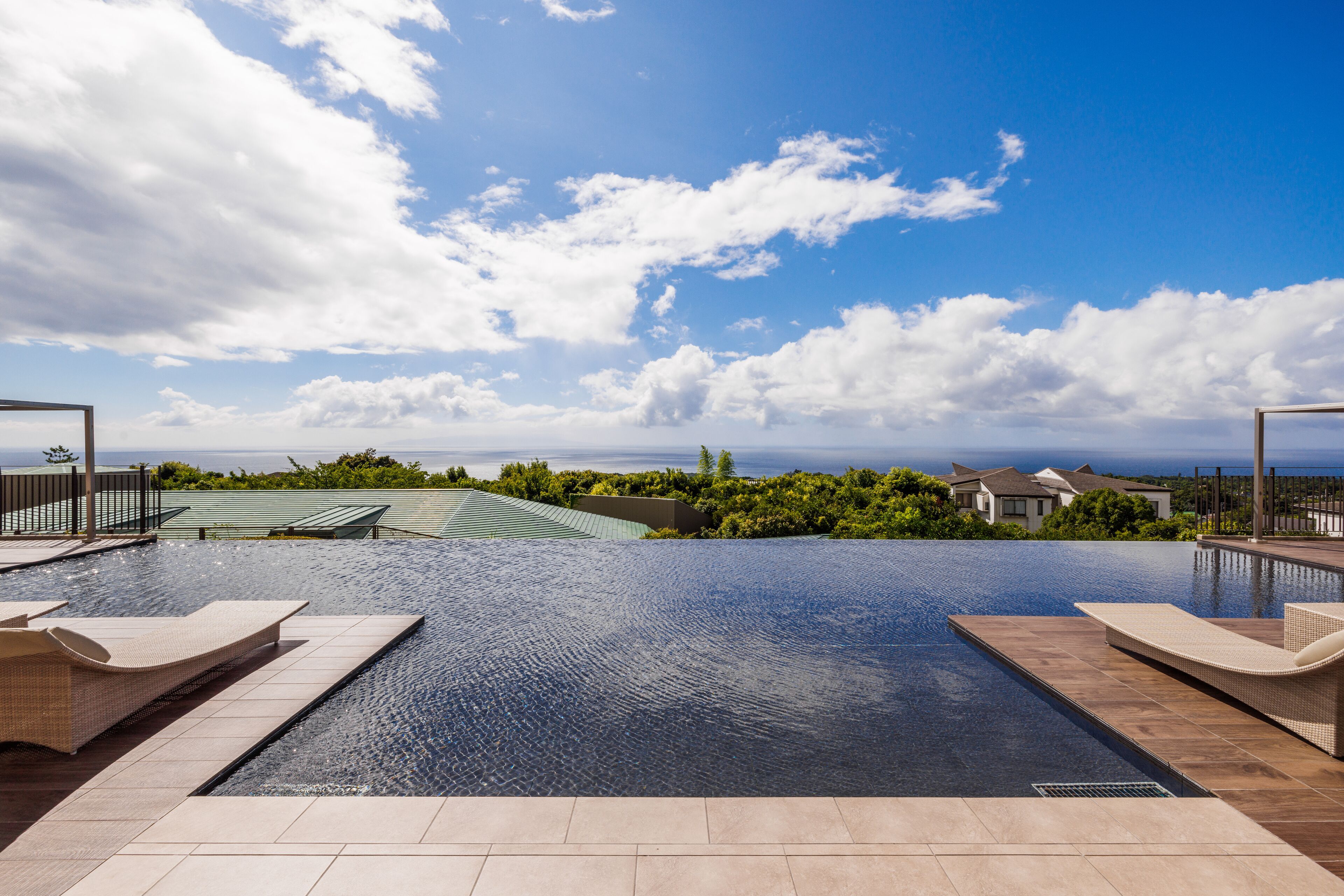 Una piscina con sillones de descanso, vista a casas y cielo despejado.