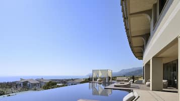 Relax in a serene outdoor space with a panoramic ocean and mountain view, featuring a modern infinity pool and comfortable lounge seating.
