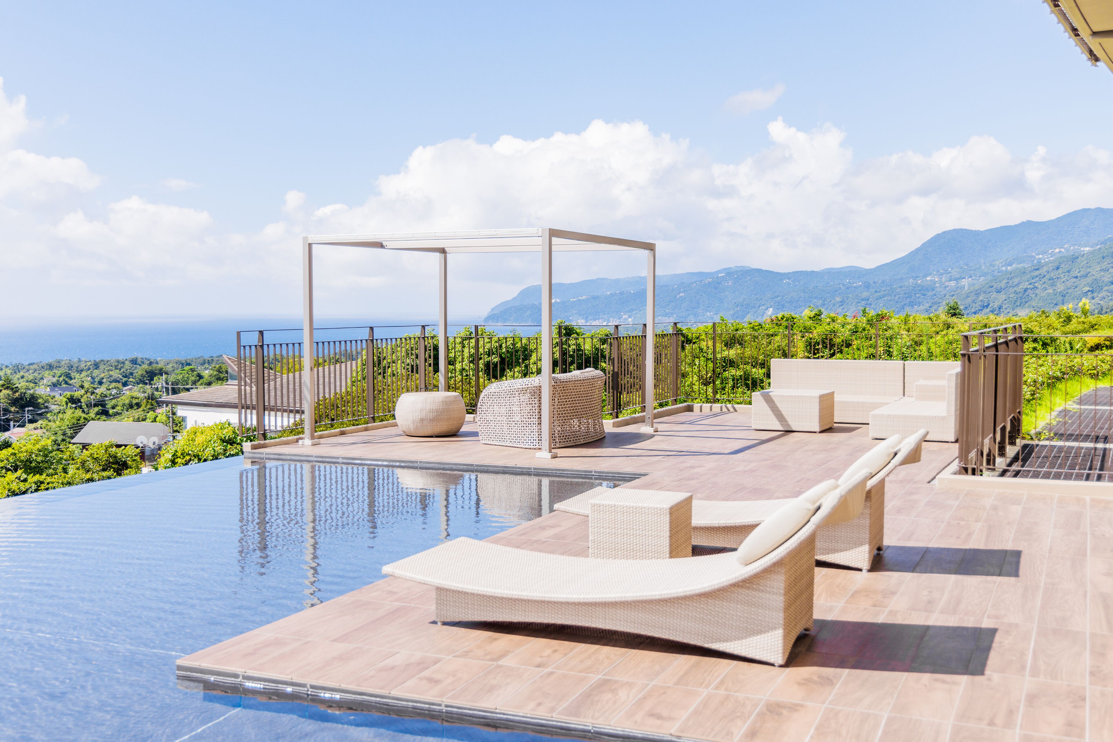 An infinity pool with lounge chairs and a pergola, overlooking a mountainous landscape.