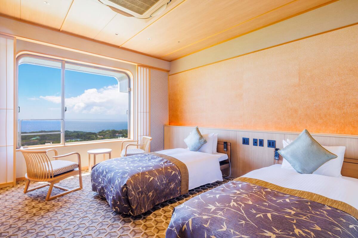Une chambre d’hôtel avec deux lits, une fenêtre donnant sur un beau paysage, une chaise et une petite table.