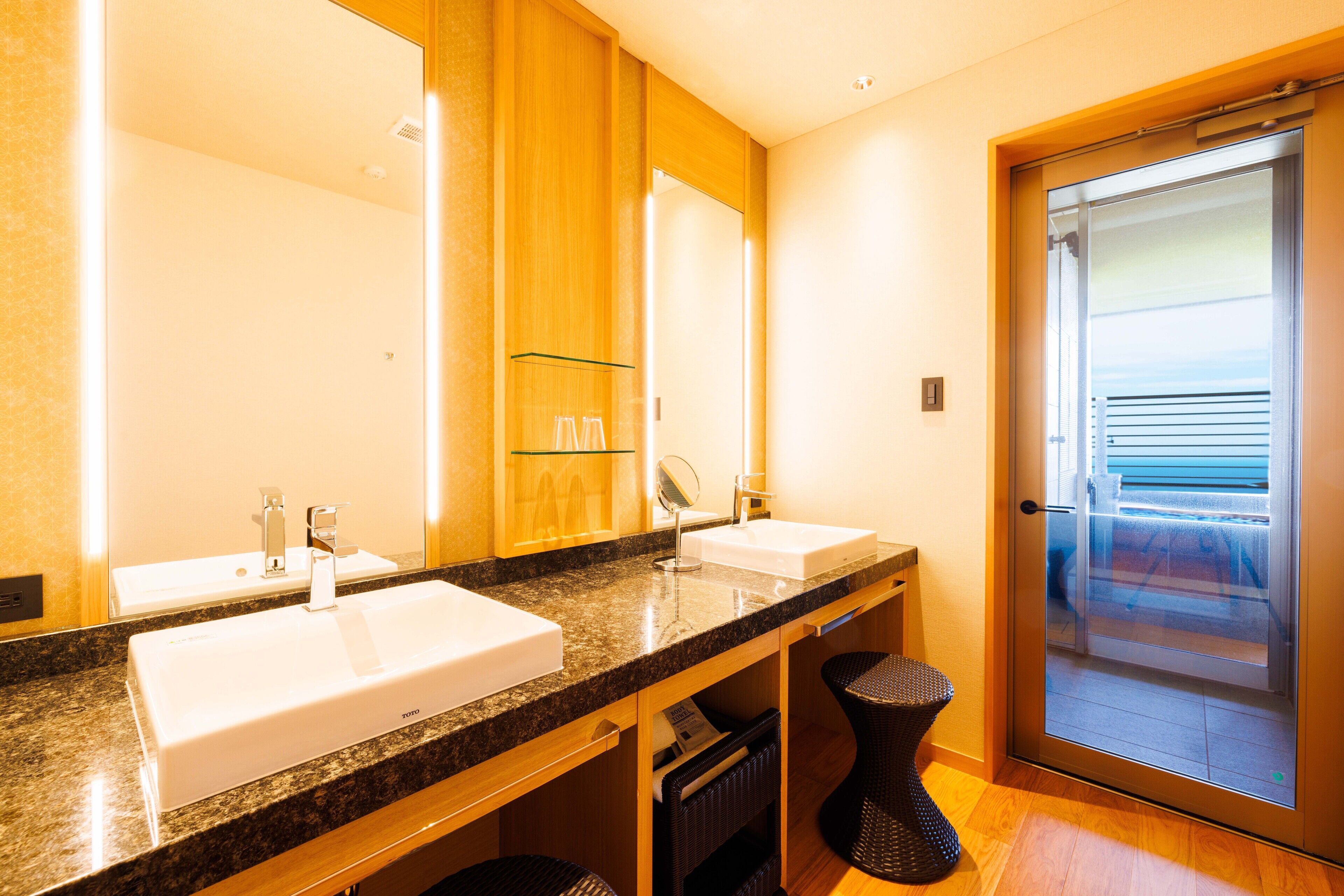 A modern bathroom with two sinks, a large mirror, and a glass door leading to a balcony.