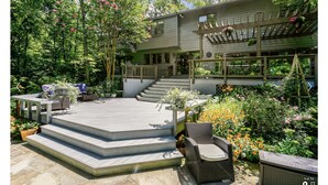 Una casa con un porche cubierto, mobiliario de exterior y un jardín con diversas plantas y flores.