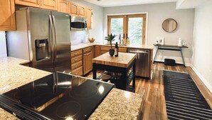 Una cocina moderna con gabinetes de madera, electrodomésticos de acero inoxidable, encimera de granito y una ventana con vistas a árboles.