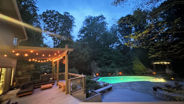 Terraza exterior con piscina, muebles de madera y luces colgantes.