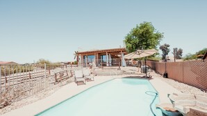 A swimming pool with a wooden deck and lounge chairs, surrounded by a fence and a large tree. - Lake view, Pool, 2 miles to Bridge, 12 ppl (Lake Havasu City)