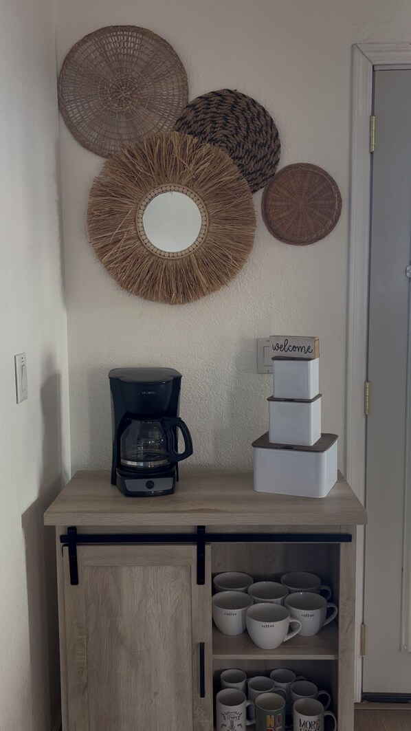 Une petite cuisine équipée d’une machine à café, d’une pile d’appareils électroménagers blancs et d’une pancarte « Bienvenue ».