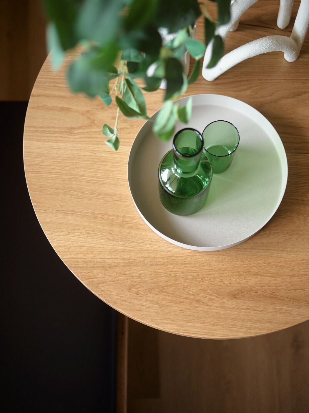 Une table ronde en bois sur laquelle repose une assiette blanche, elle-même supportant deux vases en verre vert.