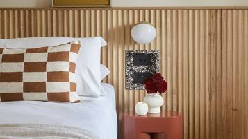 A neatly arranged bedroom with a bed, pillows, a bedside table with a vase of flowers, and a wall-mounted artwork.