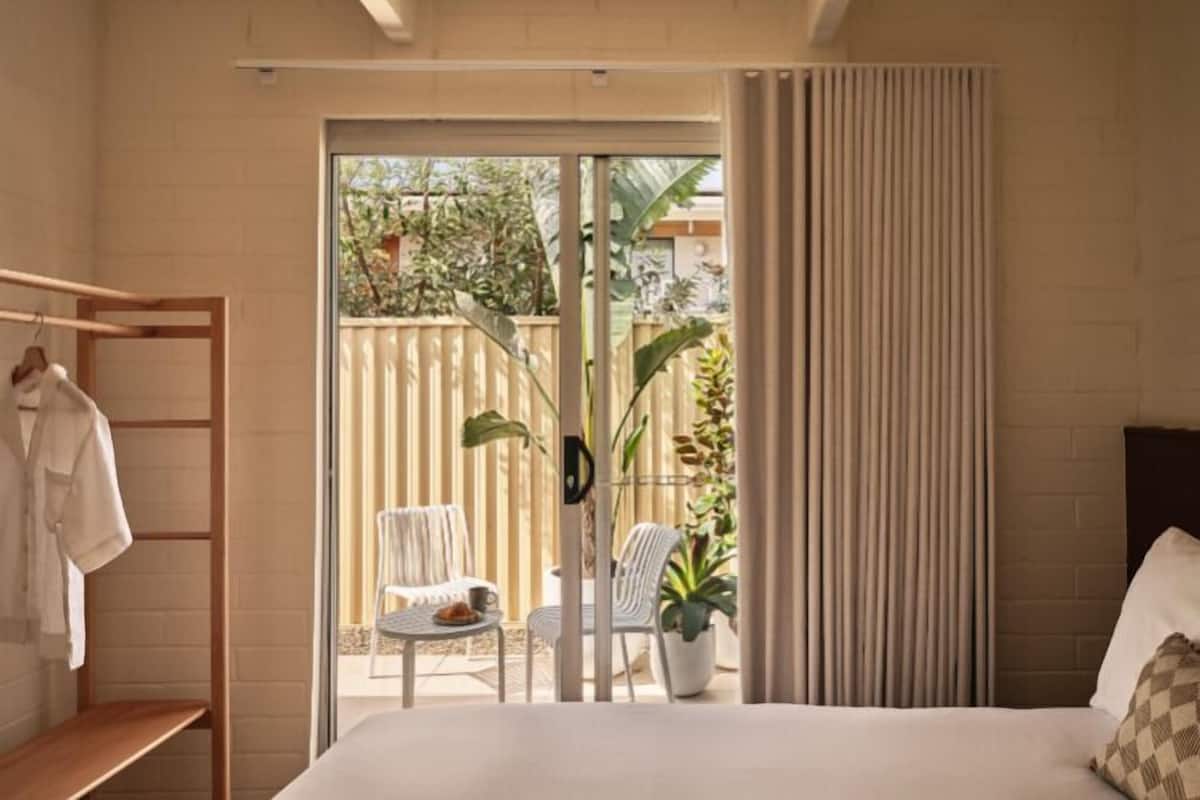 Un dormitorio con cama, armario, balcón con sillas y una planta en maceta.