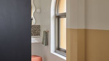 Een badkamer met een witte betegelde muur, een raam met een gebogen boog, een roze kruk en een handdoek aan een rek.