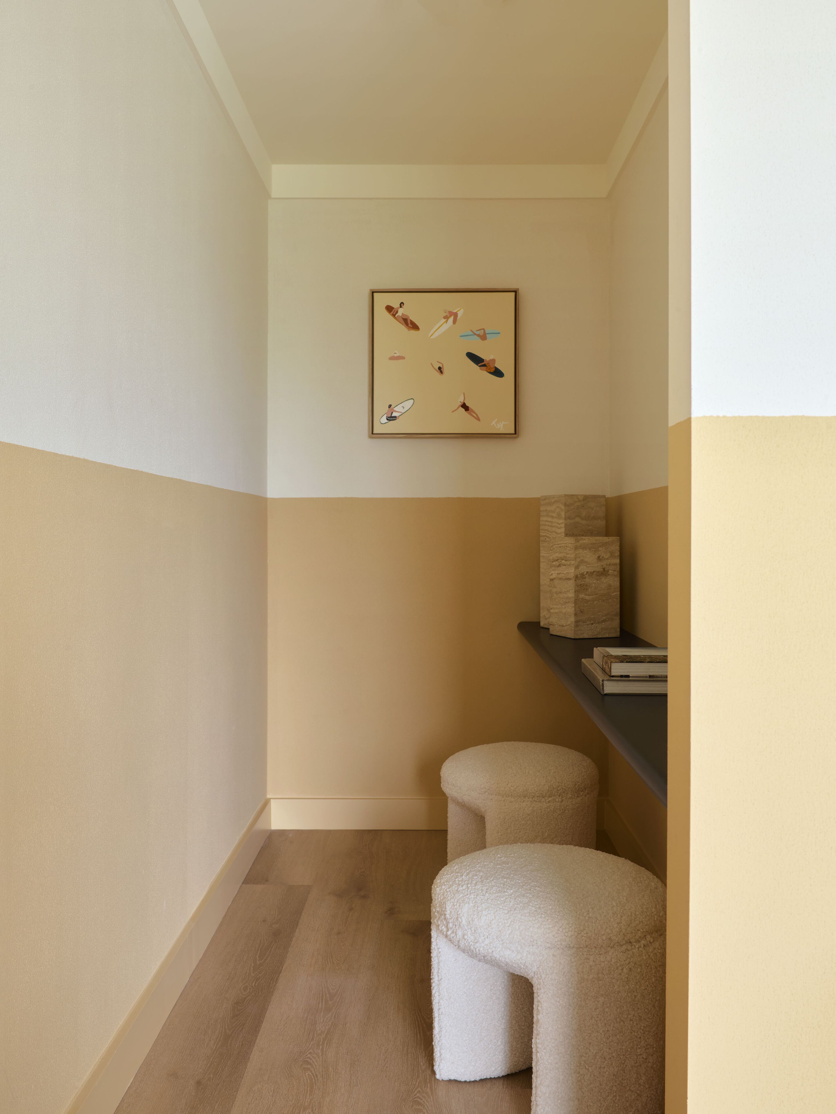 En hall med en färgskala i beige och vitt, ett inramat konstverk på väggen och två pallar.