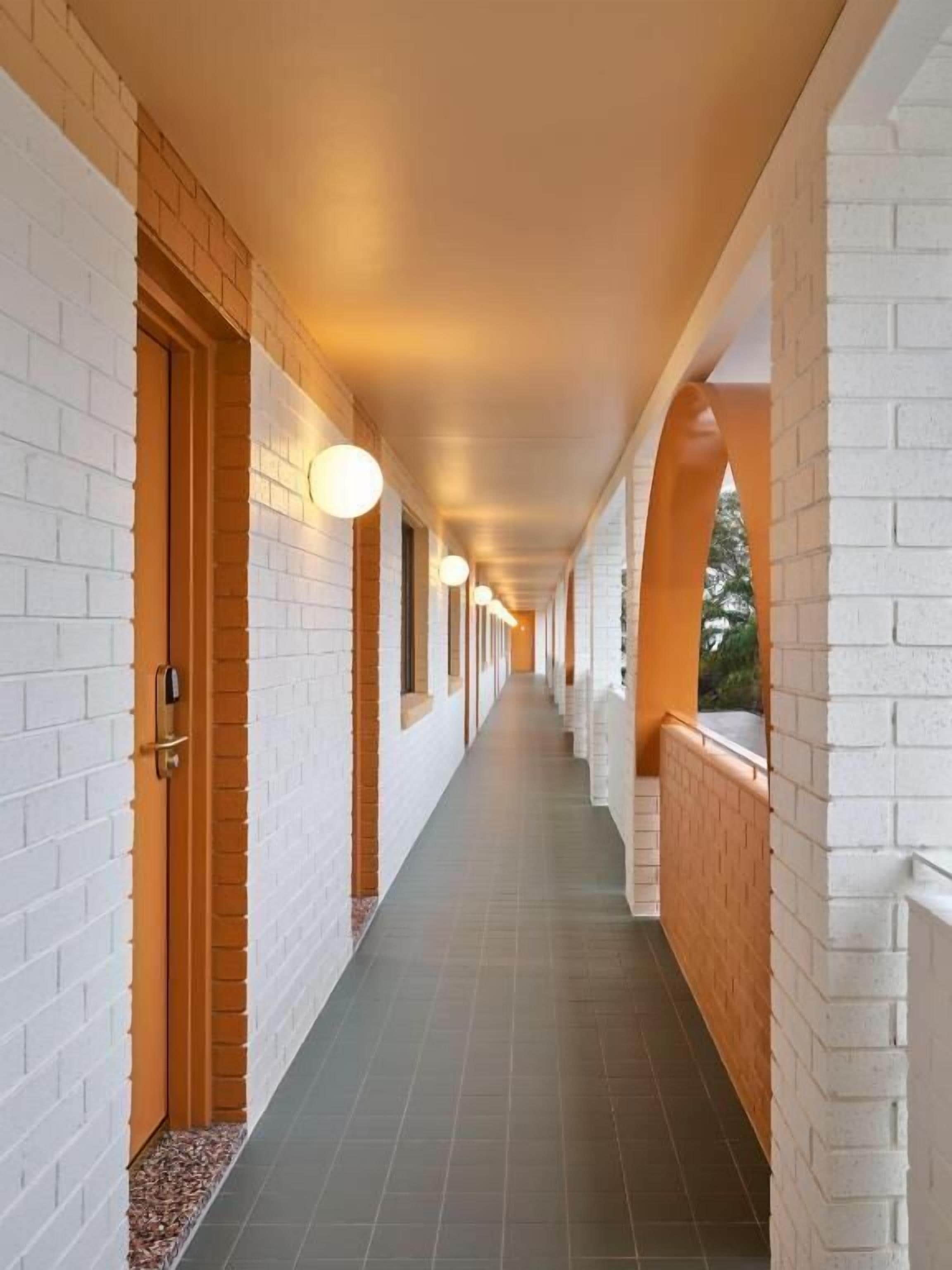 A corridor with white brick walls, wooden doors, and a tiled floor.