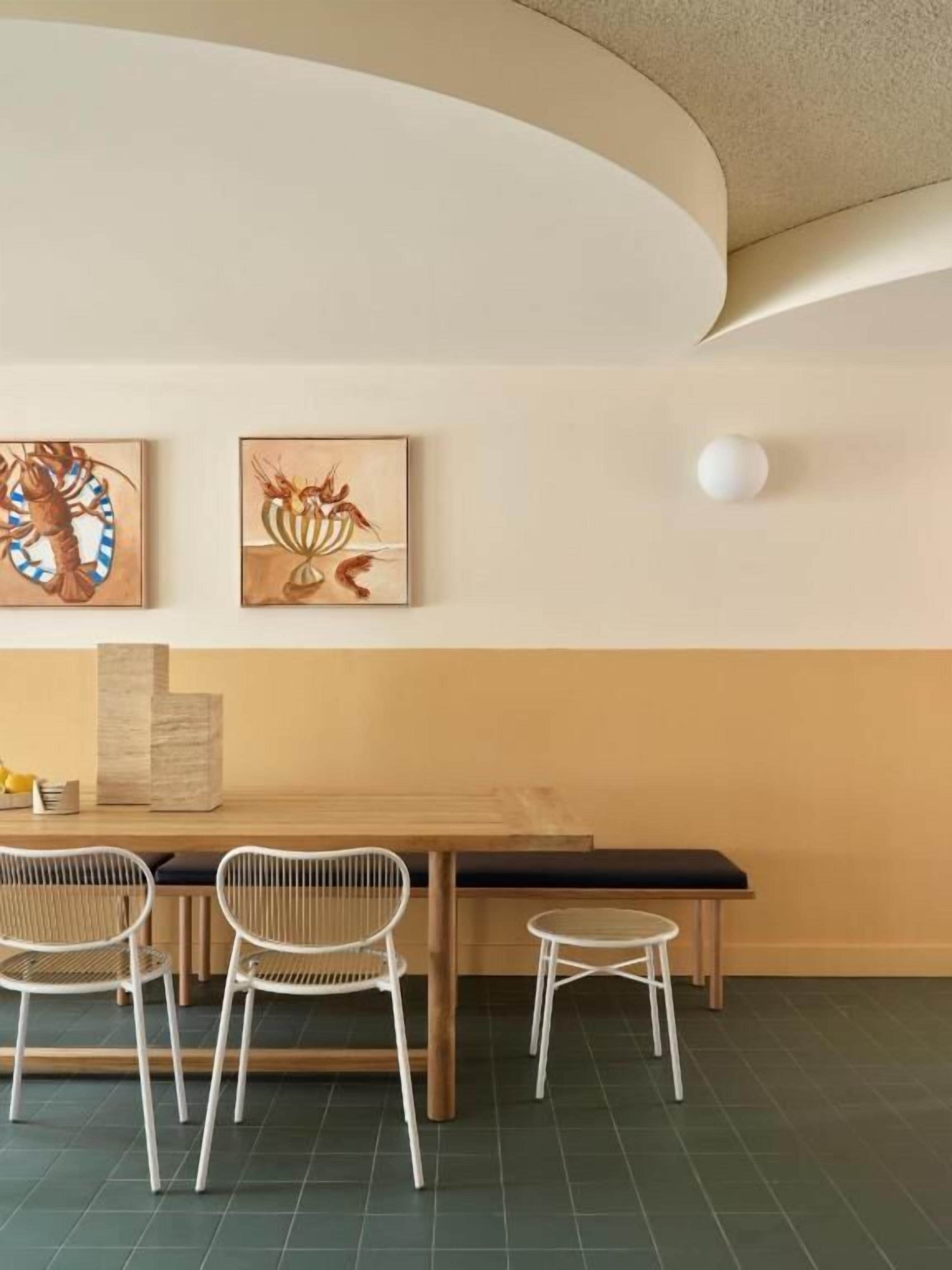 Uma sala de jantar com uma mesa de madeira, três cadeiras brancas e dois quadros pendurados na parede.