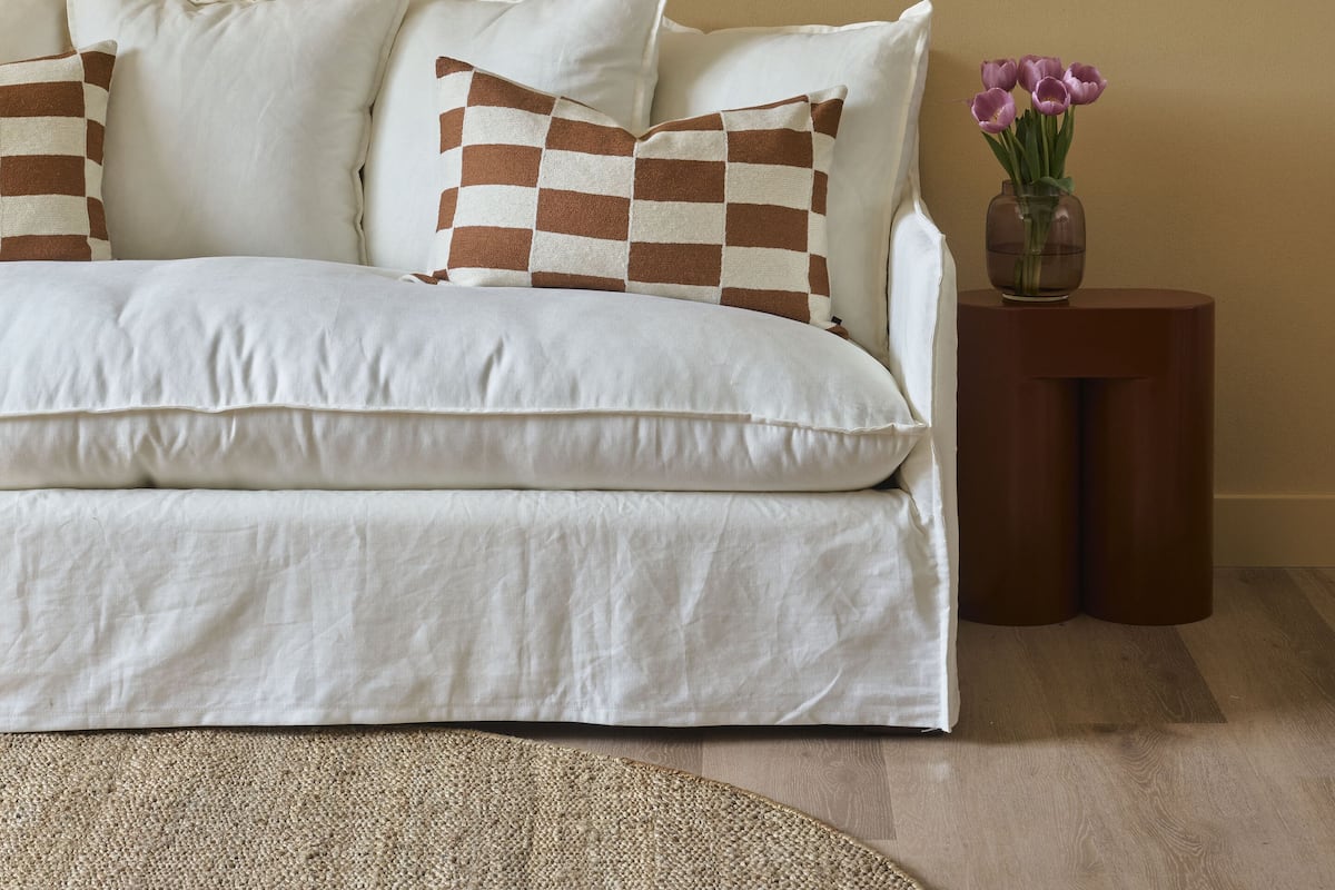 Un dormitorio con cama, almohadas, una mesita con un florero y un cuadro en la pared.