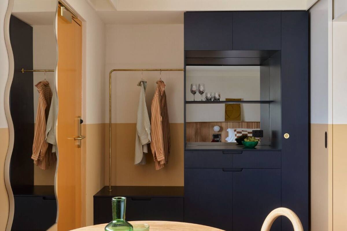 Un baño moderno con un espejo curvo, un mueble tocador de madera y una mesa redonda con un vaso verde y un plato blanco.
