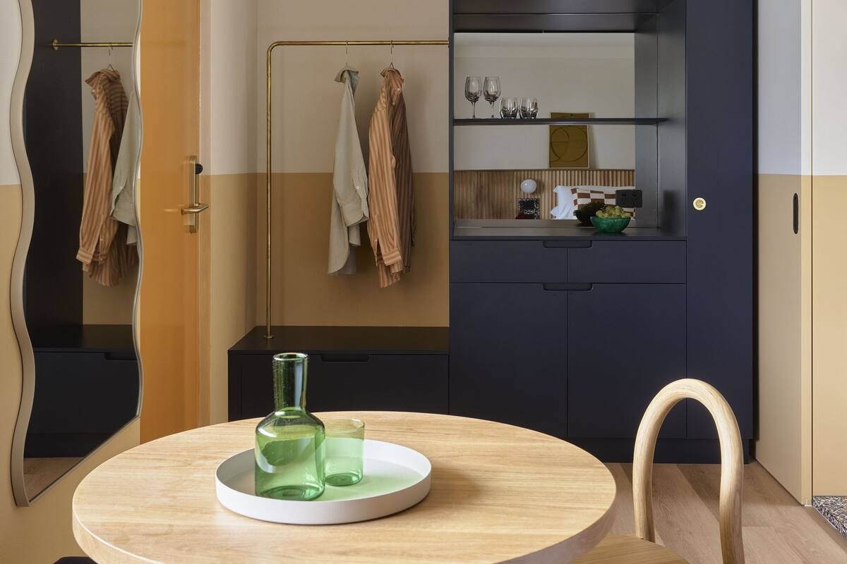 Un baño moderno con una mesa redonda de madera, un espejo con marco ondulado y un mueble azul oscuro con repisa de vidrio.