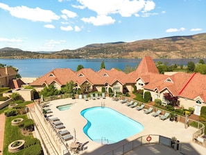 A resort with a swimming pool, lounge chairs, and a view of a lake and mountains.