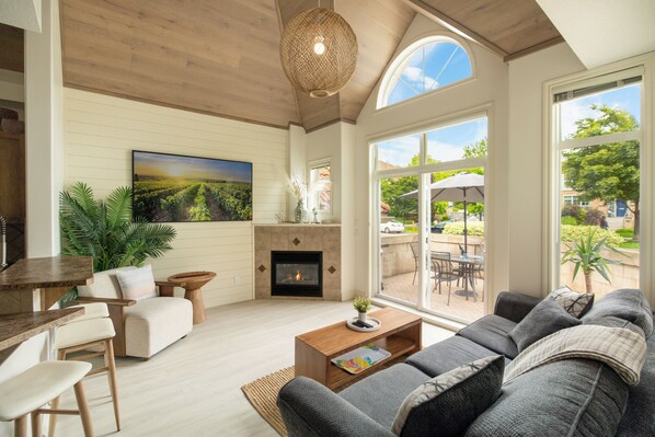 A spacious living room with a fireplace, a large sofa, a dining area, and a view of the outdoors.