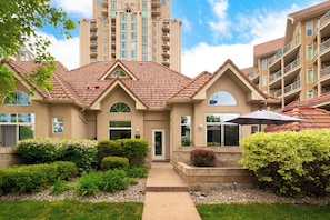 A multi-story residential building with a tiled roof, a front entrance, and a landscaped garden area.