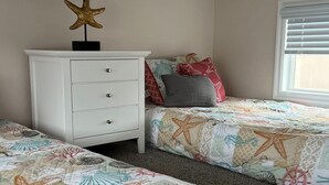 A bedroom with two beds, a white dresser, a starfish decoration, and a window with blinds.