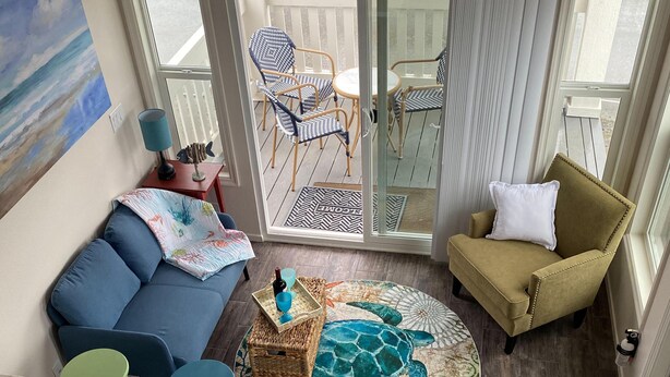 A living room with a blue sofa, a round rug with a sea turtle design, a small table with a lamp, and a chair with a cushion.