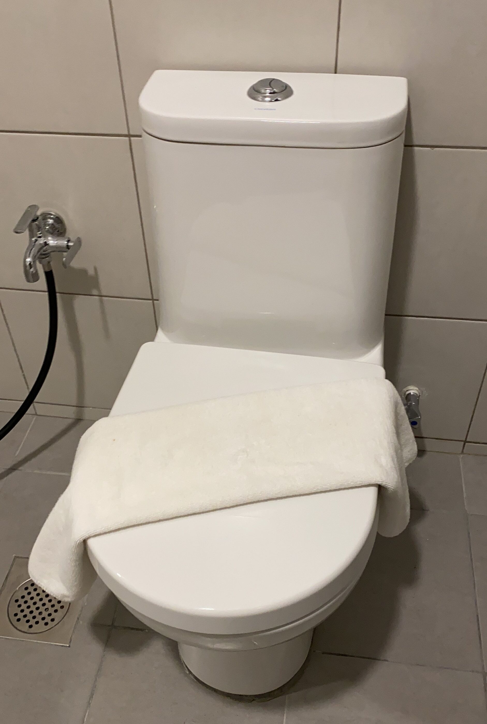 A white toilet with a closed lid, a visible flush handle, and a towel placed on the seat.